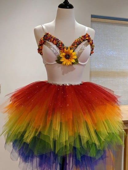 A mannequin wears a sparkly rainbow skirt and a bra with a sunflower in the middle.  