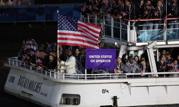 Lebron James proudly carrying the US flag for Team USA  Olympics Opening Ceremony in Paris on July 26, 2024.  The team is traveling down the Seine river in a white, two-level boat, named Bateaux Mouches.