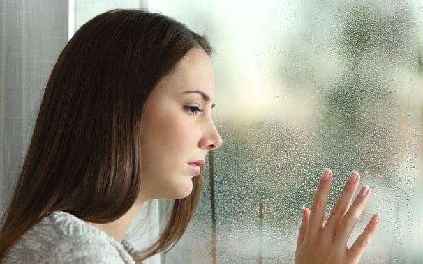 Woman sadly looking out misty window